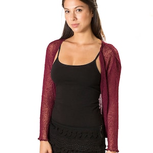 May include: A deep burgundy, long-sleeved, open-front shrug made of a lightweight, semi-sheer knit fabric. The garment features a simple, unfastened design with straight sleeves and a textured, slightly crinkled appearance throughout the material.