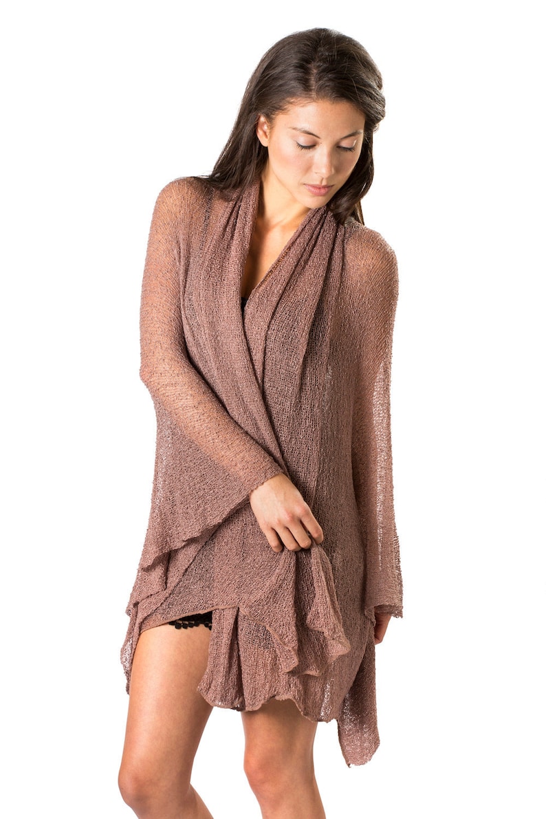 May include: A woman wearing a brown, open-front knit cardigan with a loose, flowing silhouette. The cardigan is made of a lightweight, airy fabric and has a relaxed, casual style.