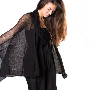 May include: A woman wearing a black sheer cardigan over a black jumpsuit. She is looking down and her long brown hair is flowing.