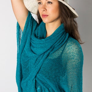 May include: A woman wearing a teal blue knitted scarf with a white wide-brimmed hat.