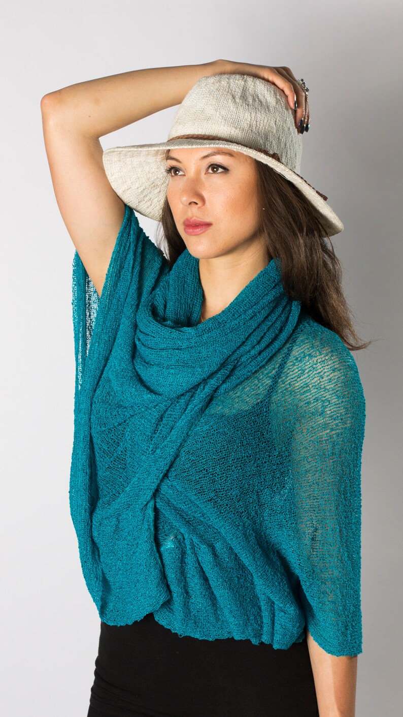 May include: A woman wearing a teal blue knitted scarf with a white wide-brimmed hat.