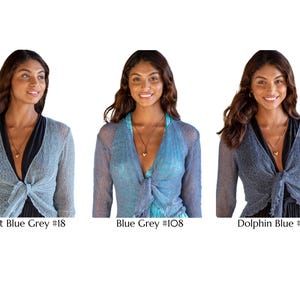 May include: Three long-sleeved, open-front shrugs with a tie-front closure. The colors are labeled as Light Blue Grey #18, Blue Grey #108, and Dolphin Blue #25. Each shrug features a sheer, textured knit fabric with a delicate, lightweight appearance.