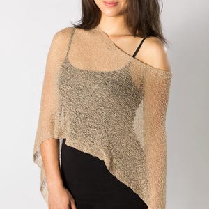 May include: A beige, open-weave poncho with an asymmetrical hemline. The poncho is draped over a black tank top and black leggings. The fabric has a subtle sheen, and the overall look is casual and stylish.