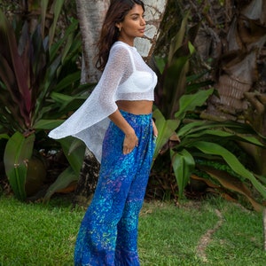 Pu&ograve; includere: Un top corto in maglia bianca trasparente con maniche larghe abbinato a pantaloni blu dal taglio ampio con una vivace stampa botanica multicolore nelle tonalit&agrave; ottanio, viola e verde, completi di tasche laterali e comodo elastico in vita.