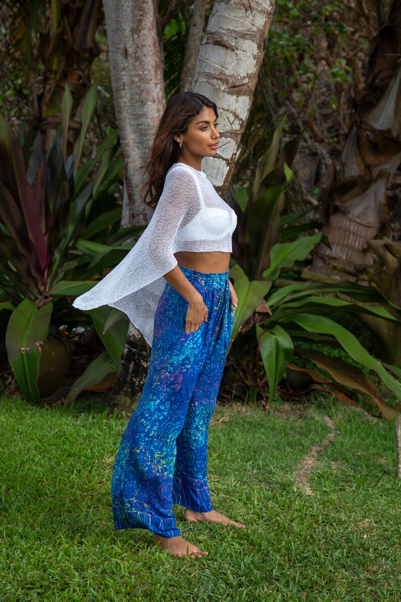 Pu&ograve; includere: Un top corto in maglia bianca trasparente con maniche larghe abbinato a pantaloni blu dal taglio ampio con una vivace stampa botanica multicolore nelle tonalit&agrave; ottanio, viola e verde, completi di tasche laterali e comodo elastico in vita.