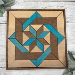 May include: A square wooden wall art piece with a geometric design. The design is made up of light brown and dark brown wood pieces, with blue accents. The piece is framed in dark brown wood.
