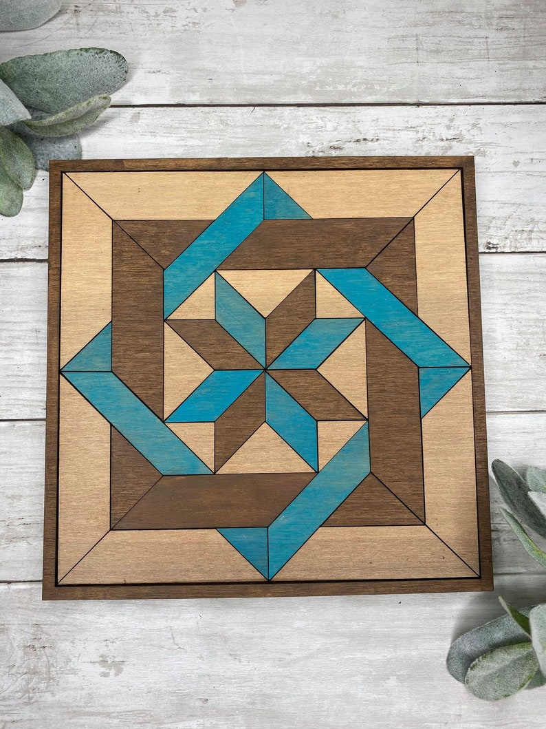 May include: A square wooden wall art piece with a geometric design. The design is made up of light brown and dark brown wood pieces, with blue accents. The piece is framed in dark brown wood.