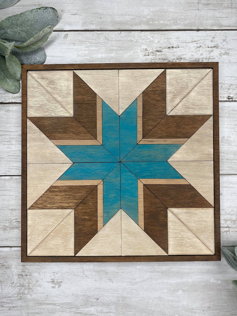 May include: A wooden wall art piece featuring a geometric star design. The star is crafted from light brown and dark brown wood, with a teal blue centre. The piece is framed in a dark brown wood frame.