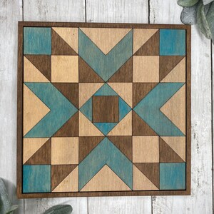 May include: A wooden wall art piece with a geometric pattern in shades of brown and blue. The design features a starburst shape with a central square.