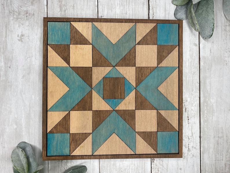 May include: A wooden wall art piece with a geometric pattern in shades of brown and blue. The design features a starburst shape with a central square.