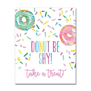 Puede incluir: Una tarjeta blanca con un diseño de donut rosa, verde y amarillo. La tarjeta dice "Donut Be Shy! Take a Treat!" y "Paperie Off Park" en la parte inferior.