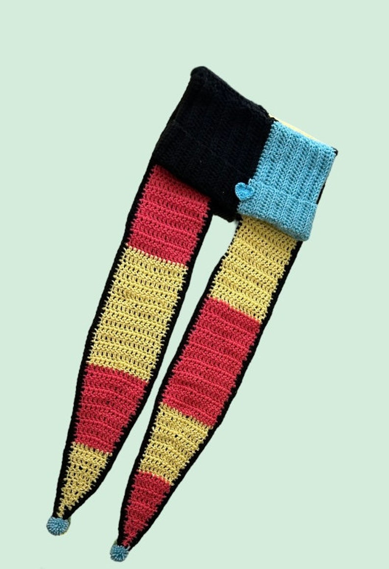 May include: A long crocheted scarf with stripes of yellow, pink, and blue. The scarf is made of a soft, textured yarn and has a unique, colorful design.
