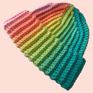 May include: A handmade, ribbed crochet beanie in a vibrant rainbow of colors. The hat transitions from pink to orange, yellow, green, and finally, teal. The folded brim and textured stitch create a cozy, stylish accessory.