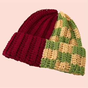 May include: A handmade beanie hat with a unique color block design. One half is a solid deep red, while the other features a checkerboard pattern of green and tan. The hat is made of a thick, textured yarn, perfect for cold weather.