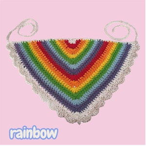 Puede incluir: Un pañuelo triangular de ganchillo con rayas horizontales en rojo, naranja, amarillo, verde, azul y morado. La pieza está rematada con un borde festoneado blanco e incluye dos finas cintas de ganchillo en las esquinas superiores. La palabra rainbow aparece debajo.