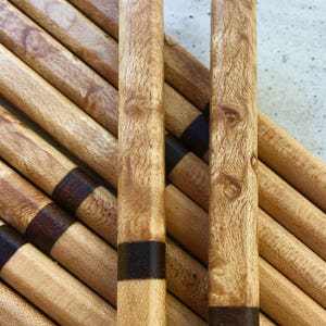 Puede incluir: Un juego de palillos de madera con un acabado de madera marrón y natural. Los palillos tienen una banda marrón oscura cerca de la parte superior.