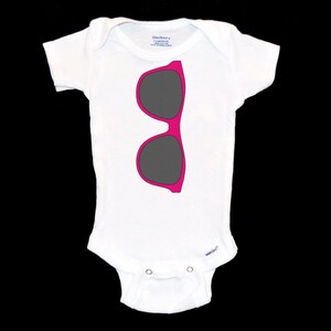 May include: White baby onesie with a pink and gray sunglasses graphic.