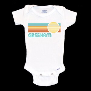 May include: White baby onesie with a retro-style graphic design featuring a sun and the word "GRESHAM" in turquoise.