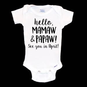 May include: White baby onesie with black text that reads "hello, mamaw & papaw! See you in April!"