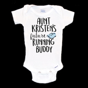May include: White baby onesie with black text that reads "Aunt Kristen's future running buddy" with a pair of blue running shoes.
