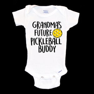 May include: White baby grow with black text that reads "Grandma's Future Pickleball Buddy" and a yellow pickleball graphic.