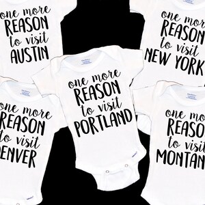 May include: Five white baby onesies with black text that reads "one more reason to visit" followed by the name of a city: Austin, Denver, Portland, New York, and Montana.