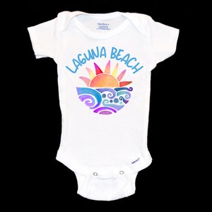 May include: White baby onesie with a colorful graphic of a sun setting over waves and the text "LAGUNA BEACH" in blue.