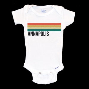 May include: White baby grow with a retro-style striped design in red, yellow, and green. The text "ANNAPOLIS" is printed in black below the stripes.