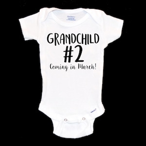 May include: White baby onesie with black text that reads "Grandchild #2 Coming in March!"