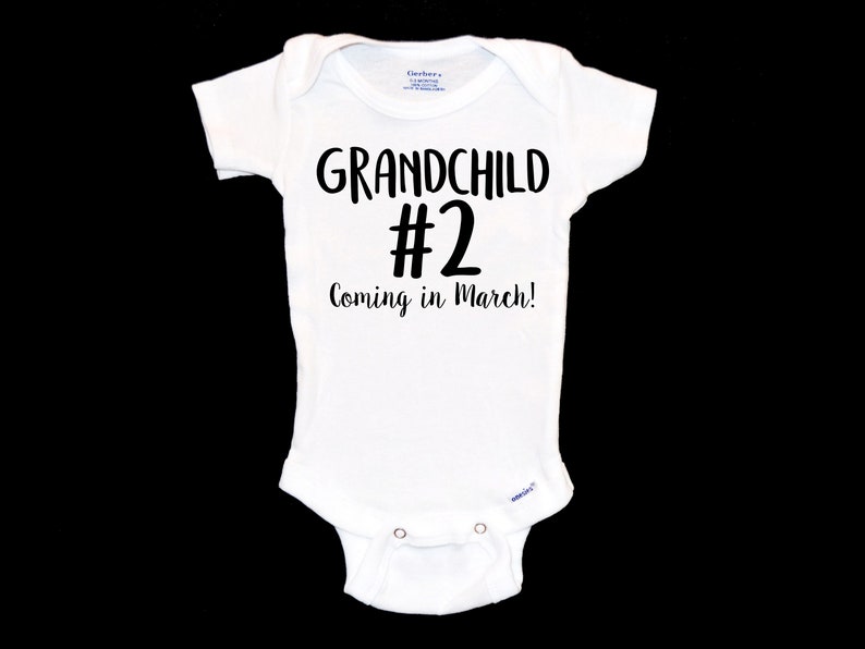 May include: White baby onesie with black text that reads "Grandchild #2 Coming in March!"