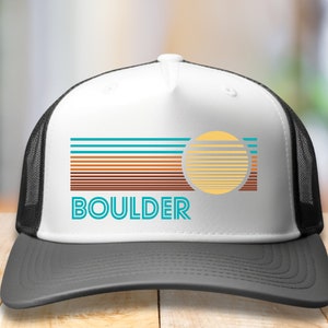 May include: White trucker hat with a black mesh back. The front of the hat features a retro-style graphic with a sun and the word "BOULDER" in blue and teal.