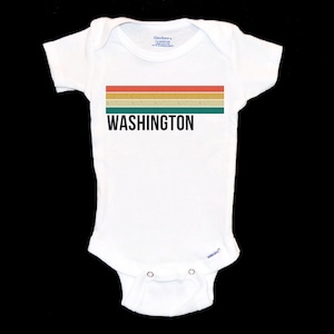 May include: White baby bodysuit featuring the word "WASHINGTON" in black. Above the text are four horizontal stripes in orange, yellow, green, and teal. The garment has short sleeves and poppers at the bottom.
