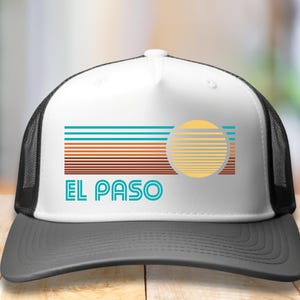 May include: A white and black trucker hat with a retro sunset graphic and the text "EL PASO" in blue and white.