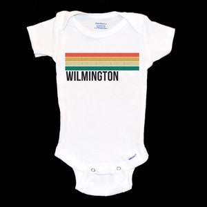 May include: White baby onesie with a retro-style striped design in red, orange, yellow, and green. The text "WILMINGTON" is printed in black below the stripes.