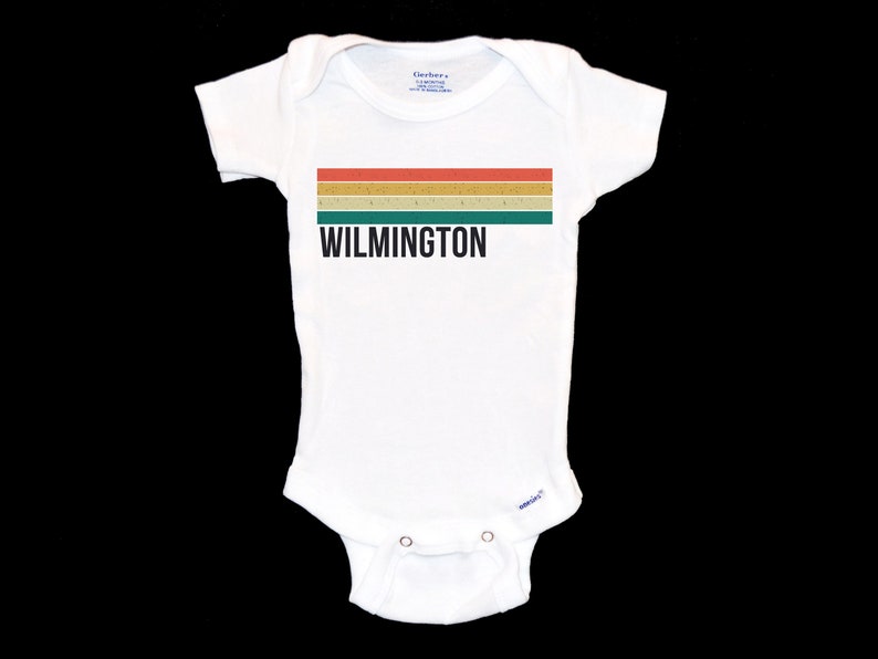 May include: White baby onesie with a retro-style striped design in red, orange, yellow, and green. The text "WILMINGTON" is printed in black below the stripes.