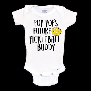 May include: White baby onesie with black text that reads "Pop Pop's Future Pickleball Buddy" and a yellow pickleball graphic.