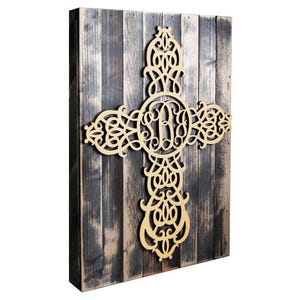 May include: A gold-coloured, ornate, wooden cross with a monogram in the centre, mounted on a rustic wooden background.