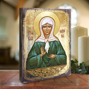 May include: A hand-painted icon of a woman with a halo, wearing a white head covering and a green robe. The icon is on a wooden background with gold accents and the text "СТАА БАК" and "МАТО НА".