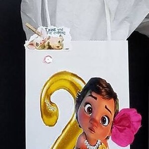 May include: A white gift bag with a gold number 2 and a cartoon character from the movie Moana. The bag has a pink flower and the text "Set #2" on the front.
