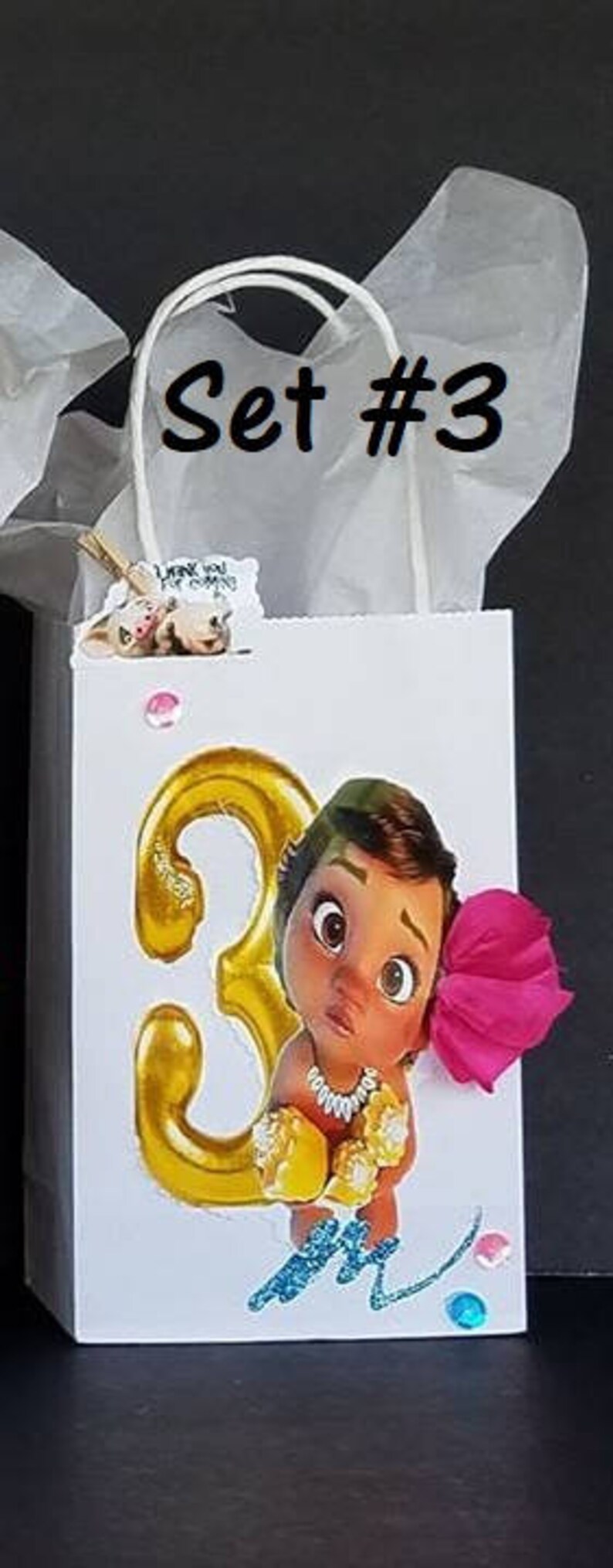 May include: White gift bag with a gold number 3, a pink flower, and a cartoon image of a brown-skinned baby girl. The bag has a white handle and the text "Set #3" is written on the front.
