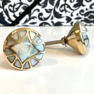 May include: Two decorative cabinet knobs with a gold finish and inlaid mother-of-pearl. The knobs have a geometric design with a central diamond shape and triangular accents. The hardware is ideal for furniture upgrades.