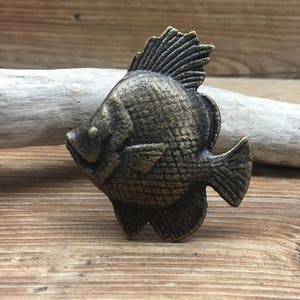 May include: A cast iron fish door knob with a distressed gold finish. The fish has a fin on its back and a detailed design.