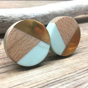 May include: Two circular cabinet knobs with a geometric design. Each knob has sections of light wood grain, mint green resin, and gold-coloured metal. The knobs are displayed on a wooden surface.