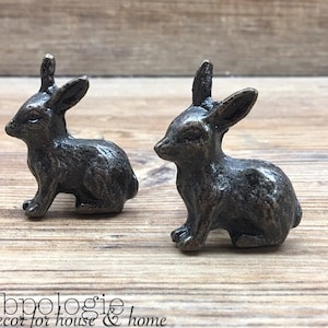 May include: Two antique silver rabbit drawer pulls. The rabbit pulls are sitting on a wooden surface.