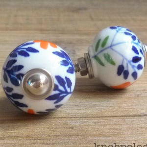 May include: Two ceramic cabinet knobs with floral designs. The knobs are white with blue leaves, orange accents, and silver hardware. The knobs are for fresh decor for house & home.