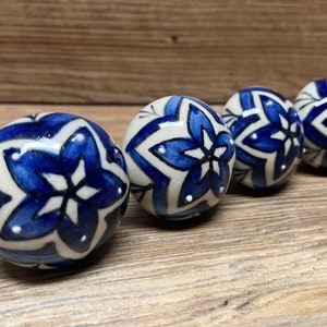 May include: Four blue and white ceramic knobs with a floral design. The knobs are round and have a glossy finish.