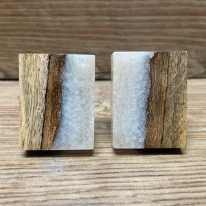 May include: Two rectangular cabinet knobs featuring a combination of natural brown wood grain on one side and a shimmering, pearlescent white resin inlay on the other. The wood and resin sections are joined by a distinct, organic, wavy edge.