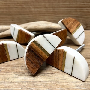 Op de afbeelding: Een verzameling halfronde kastknoppen. Elke knop combineert wit, houtnerf en messingkleurige accenten. De knoppen zijn geplaatst op een houten oppervlak, waarbij hun ontwerp en textuur worden benadrukt. Ongeveer 5 cm in diameter.