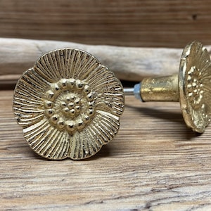 May include: Two gold-toned metal cabinet knobs shaped like flowers. Each knob features a textured, radiating petal design with a central cluster of small raised dots. The knobs have a cylindrical base and a short metal screw extending from the back.