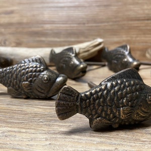 May include: Six antique bronze fish-shaped drawer pulls. The pulls have a detailed, textured finish and are perfect for adding a nautical touch to furniture.